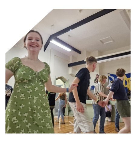 A smiling teenage girl wearing a green flowery dress with young people dancing behind her