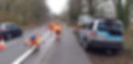 Working Men in high-visibility uniform carrying out drainage repairs on a road with cars parked.