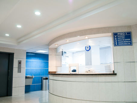 Hospital lobby with a reception desk. Blue wall with elevator and water fountain on the left.