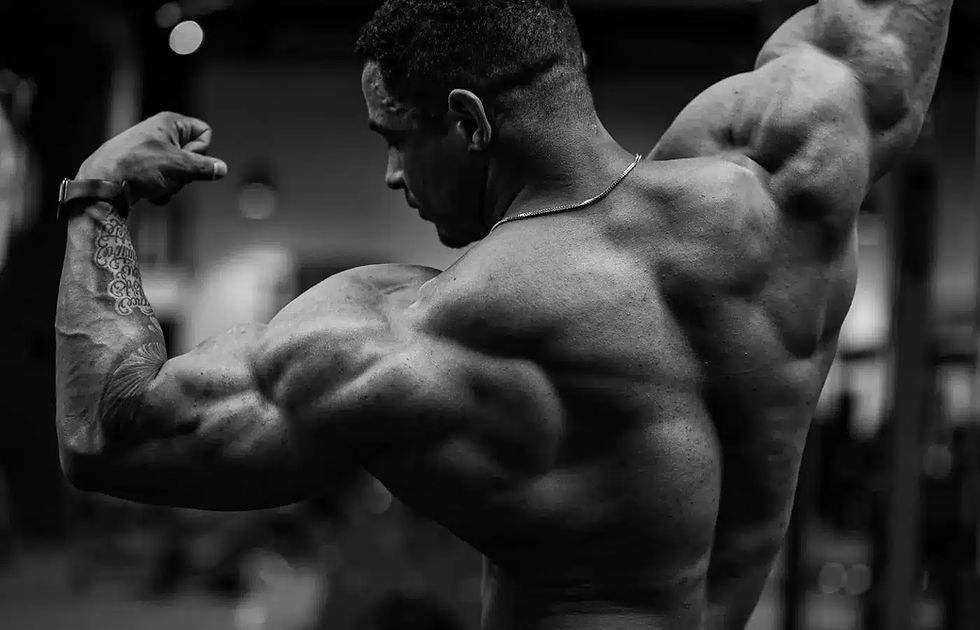 Black-and-white image of a muscular bodybuilder flexing his back and arms during an intense gym workout, highlighting strength, muscle definition, and advanced bodybuilding performance related to Buy Ultima-TNE 100 Online.