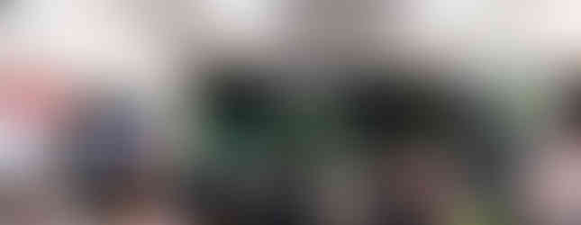 Crowd of guests gathered inside the Mt Martha GolfSim venue during the grand opening event, with green balloons, simulator screens, and signage visible in the background.