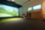 Luxury indoor golf simulator installation with Uneekor technology, widescreen impact screen, dual monitors, and putting mat, featuring a dog sitting beside the setup.
