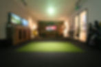 Indoor Golfsim golf simulator room with hitting mat, dual side screens, widescreen display, and golf clubs.