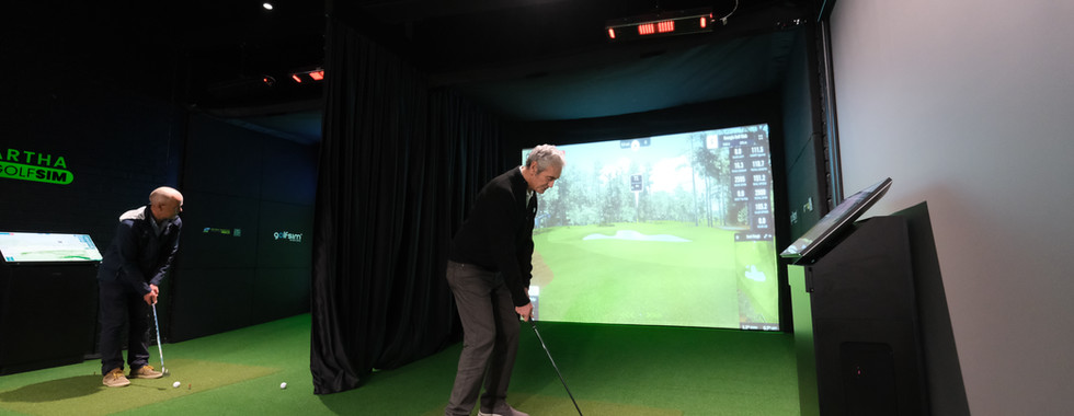 Golfer lining up a shot inside the Mt Martha dual-bay simulator room, with GSPro virtual course display and touchscreen control panel nearby.
