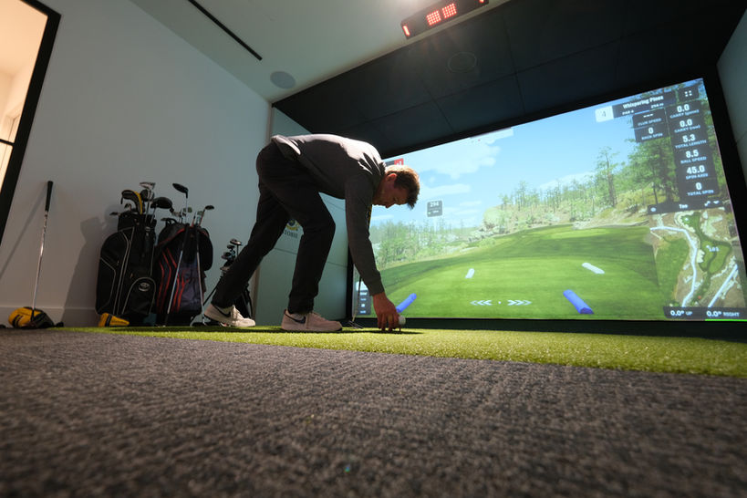 Golfer teeing up in front of GSPro projection screen with full turf flooring and custom golf bag setup — indoor golf simulator by Golfsim Australia.