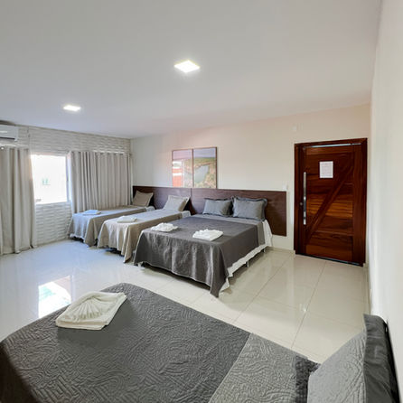 A beleza da imperfeição natural destaca-se na cabeceira de madeira maciça com bordas vivas e irregulares, que ancora a decoração do quarto. Sobre o banco rústico lateral, um vaso de vidro com gérberas brancas e uma vela aromática compõem uma atmosfera de pureza e design orgânico, harmonizando com a roupa de cama em tons de cinza suave.