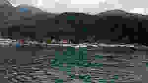 Foto da Ilha Grande. Em primeiro plano vemos um mar calmo e mais ao longe barcos de pesca atracados na areia da praia. Ao fundo montanhas cobertas por vegetação.