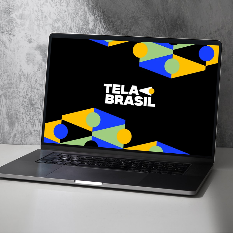 Um laptop cinza-metálico aberto está posicionado em uma superfície branca contra uma parede de concreto texturizado, exibindo na tela um design de marca vibrante sobre um fundo preto. No centro da tela, o logotipo da 'TELA BRASIL' aparece em letras brancas ousadas, acompanhado por um pequeno ícone de seta amarela. O design da tela é cercado por um padrão dinâmico de formas geométricas e círculos em azul, amarelo e verde, refletindo as cores da bandeira brasileira.
