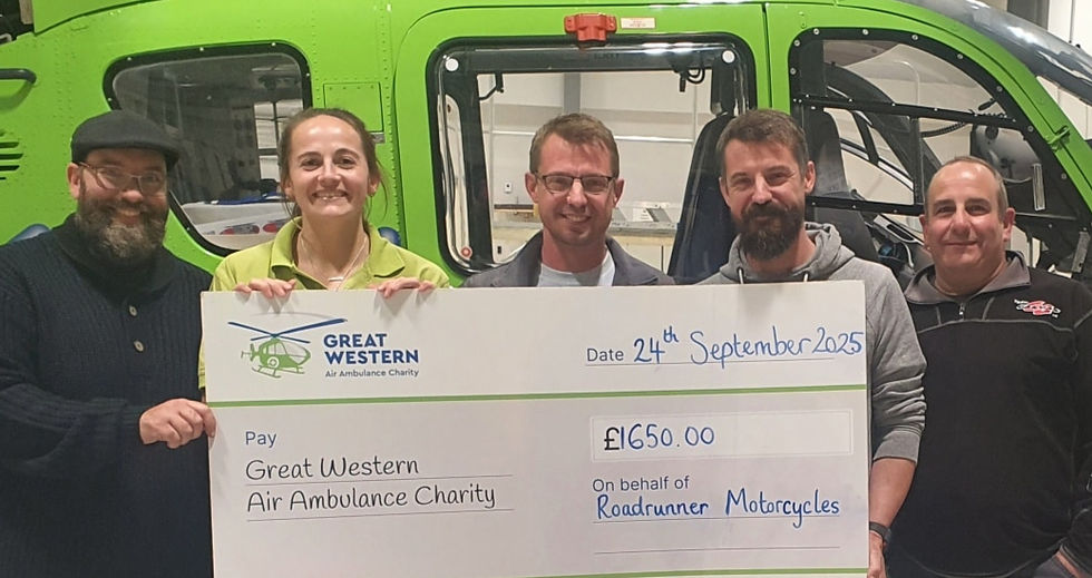 Five people smiling, holding a large charity check for £1650 dated 24th September 2025, in front of a green helicopter. Mood is cheerful.