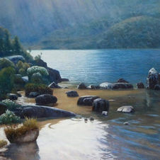 Atmsopheric light and reflections on waters of Dove Lake with rocks and soft blue mountains in the distance. Tasmanai