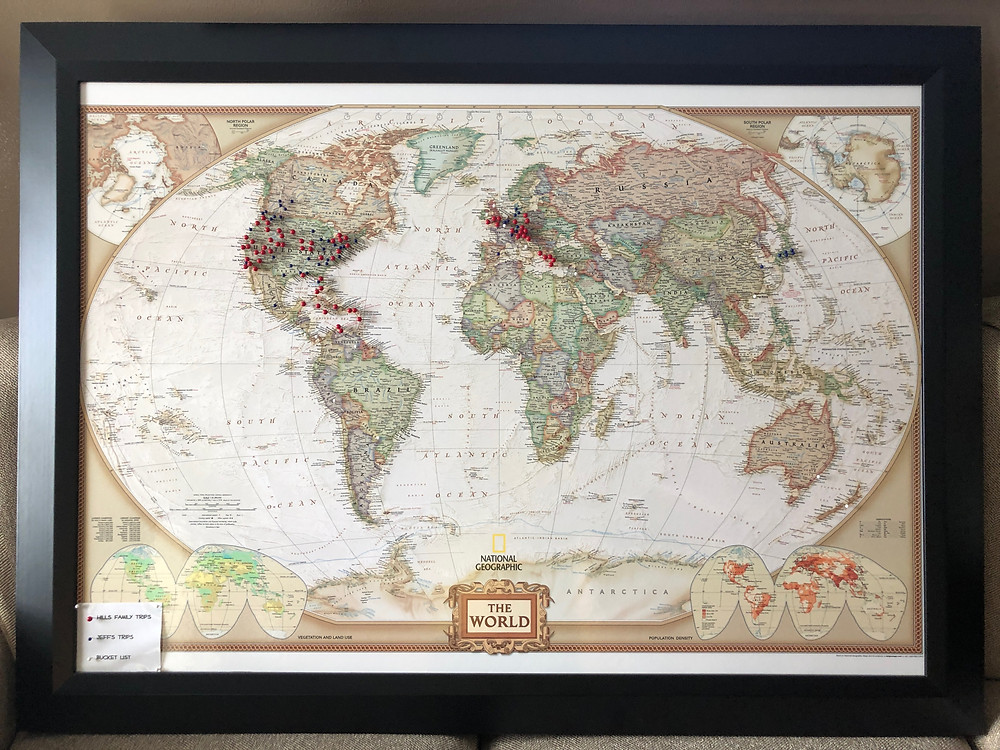 Framed world map, with blue, red or white pins placed at locations we have traveled or bucket list items we hope to travel to