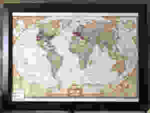 Framed world map, with blue, red or white pins placed at locations we have traveled or bucket list items we hope to travel to