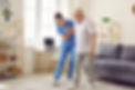 Young nurse helping elderly man walk in the room, holding his hand, supporting him. Treatm