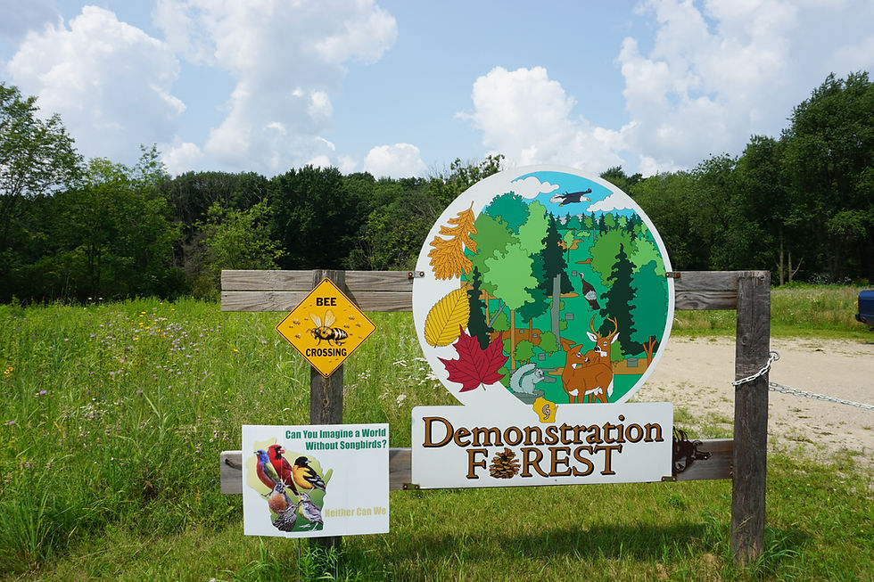A sign for the demonstration forest is shown with a prairie and woods in the background.