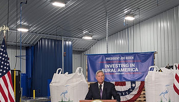 A man stands behind a podium. There is a blue banner behind him that reads, "Investing in Rural America."