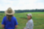 Two people stand in a field talking to each other.