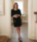 Frankie casually standing in doorway. She is wearing a dark sweater dress, holding a mug, and smiling at the camera.