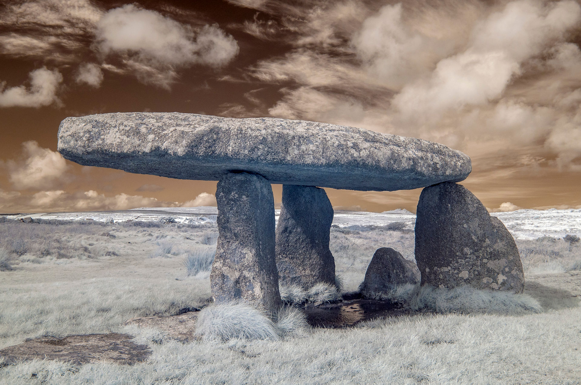 A seemingly precariously balanced, yet sturdy, ancient dolmen against a field of white grass and a dark orange sky.