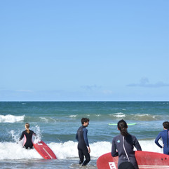 Instructores y alumnos disfrutando de una clase de surf en el agua, con olas suaves y un cielo despejado en la costa de Marruecos.
