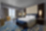 Modern hotel room with large bed, blue bench, desk, and bay view