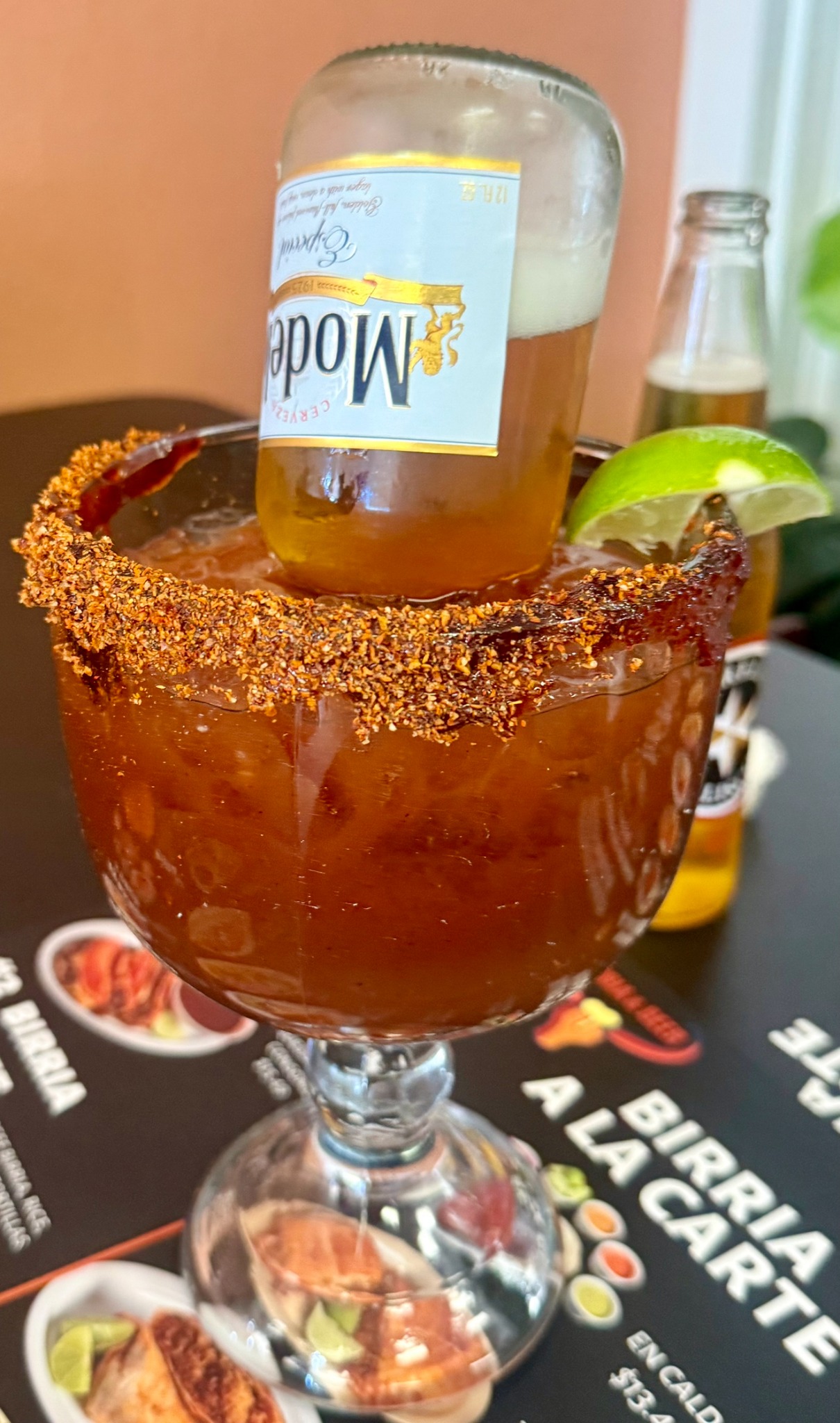 Birria & Beer michelada with a seasoned rim, lime and beer bottle