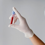 hand wearing a white medical glove holding a blood vial