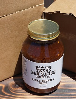 A bottle of spicy apple bourbon barbecue sauce displayed on a rustic table beside its shipping box and packing material.