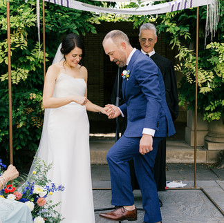 Bride and groom holding hands under a floral chuppah during intimate garden ceremony