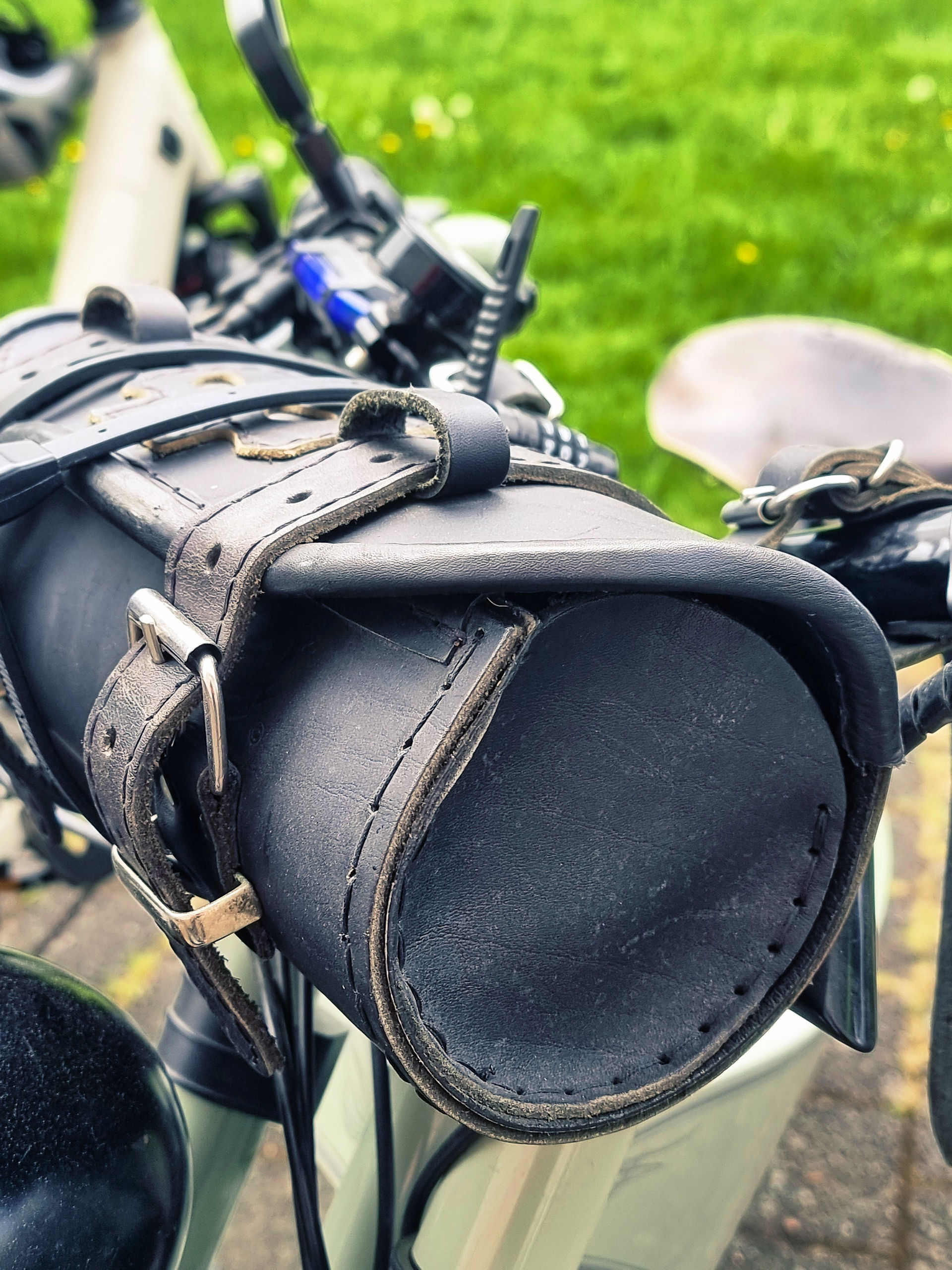 Nahaufnahme einer braunen Leder‑Lenkertasche mit Schnallen an einem Cruiser‑Bike, fotografiert im Grünen am Hafen.