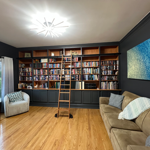 Room with bookshelves, ladder, couch, and armchair.