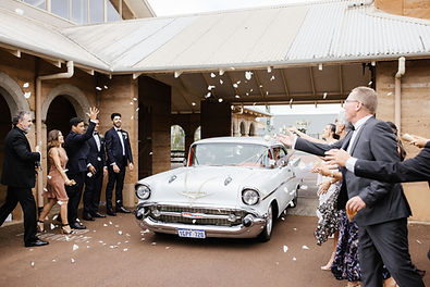 A joyful wedding moment as the newlywed couple departs from their church ceremony in our classic white 1957 Chevrolet.