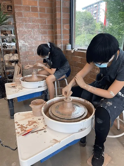 Youth pottery students throwing off the hump, a wheel technique for throwing small objects.