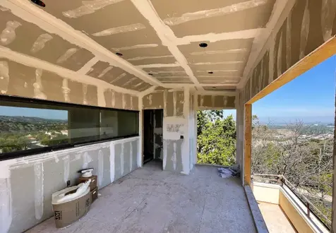 Interior of room addition with installed drywall, large windows, and scenic hillside views.