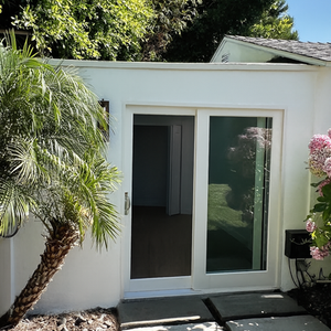 Custom-built ADU with white exterior, sliding glass door, and landscaped entry path completed by professional contractors.