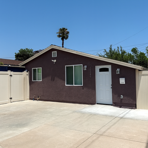 Exterior view of a newly converted ADU with brown stucco finish, white entry door, vinyl windows, and a concrete driveway, completed by ILMA TRADE SERVICE USA construction company.