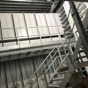 På bildet vises deler av en metalltrapp og delvis ferdig monterne metallreoler. Noen løse ledninger synes på enden av reolene. 