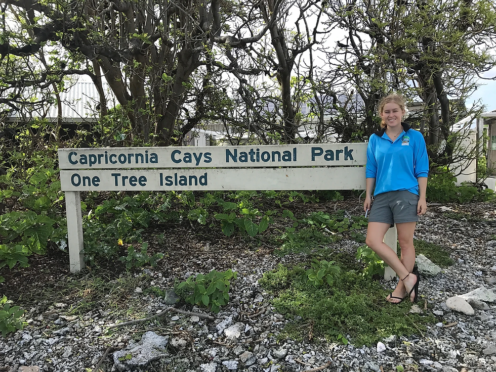 Woman standing in front of wooden sign that reads "Capricornia Cays National Park One Tree Island."