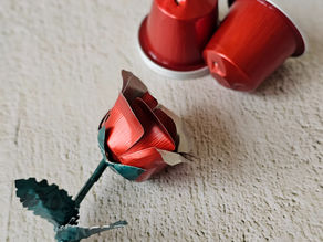 A red rose upcycled from aluminium coffee pods next to red coffee pods on a white background