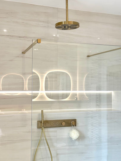 Large walk in shower with brushed brass shower head and valve.