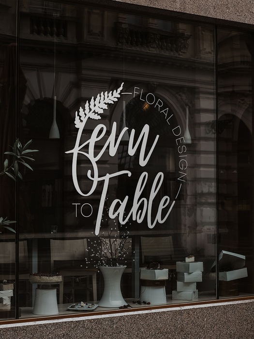 Custom logo visually displayed in a translucent white on storefront windows. The logo is for Fern to Table and include an F made of a fern and text arched around the outside.