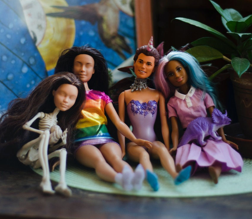 four barbie dolls on top of the table, all in queer outfits