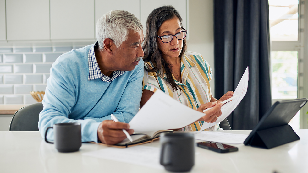 Couple sitting in kitchen with cups of coffee doing research with laptop and paperwork