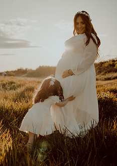 Pregnant woman sunset in grass with toddler girl kissing belly