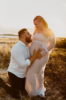 Pregnant woman sunset with husband holding stomach
