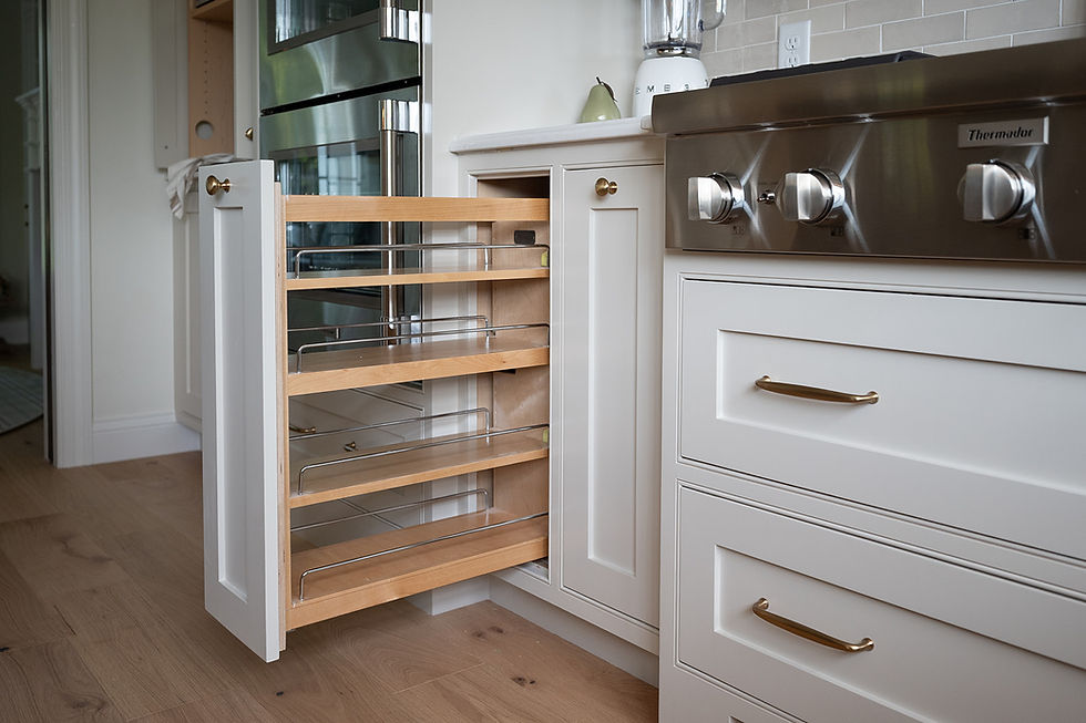 Pull-out wooden spice rack in a modern white kitchen with stainless steel appliances. Light wood floor and light walls create a cozy ambiance.