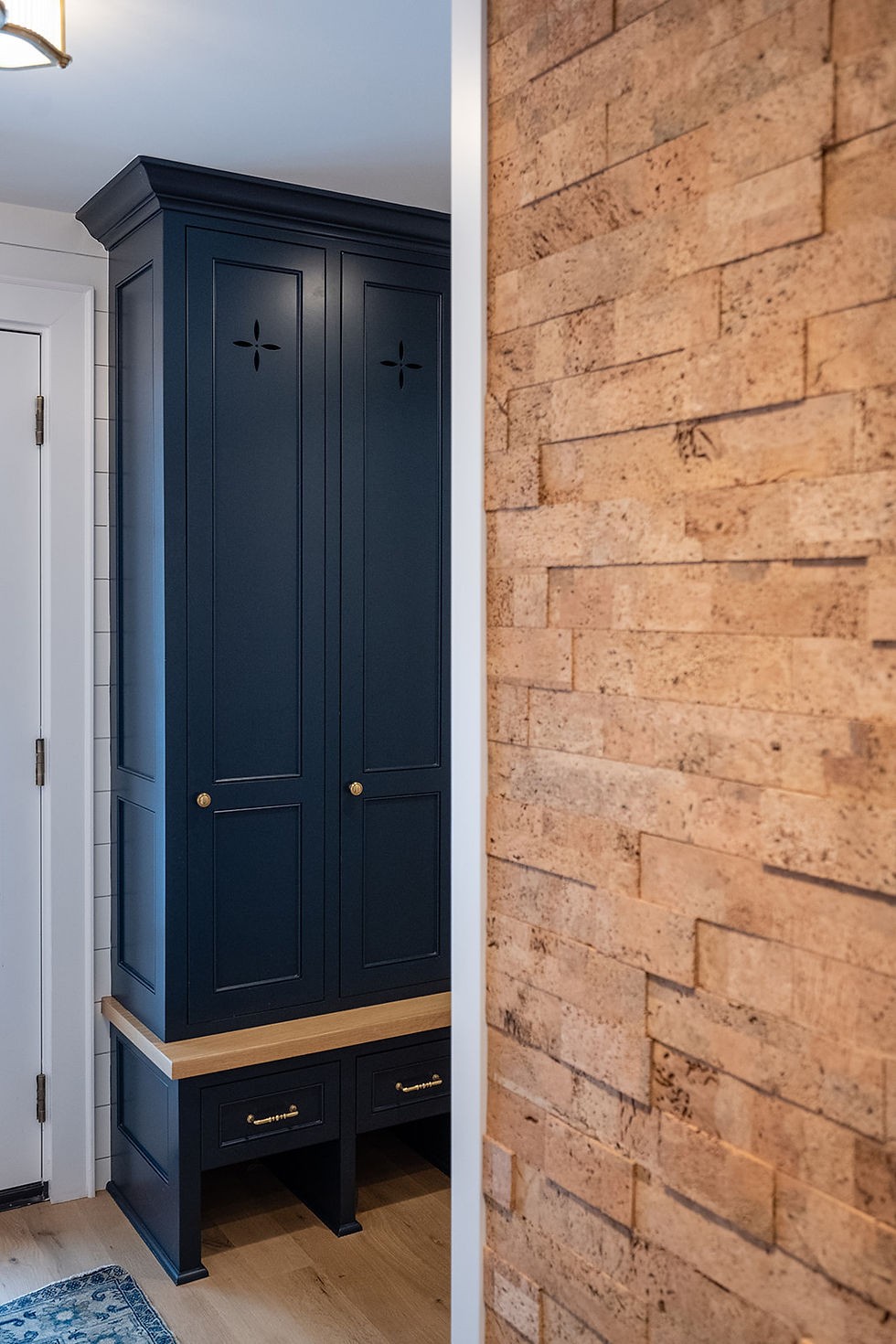 Navy built-in cabinet with brass knobs beside a tan brick accent wall in a modern interior room.