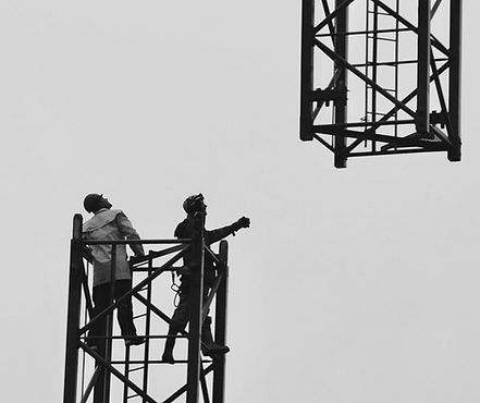 Zwei Arbeiter auf Gerüst und ein weiteres Gerüst im Hintergrund, grau.