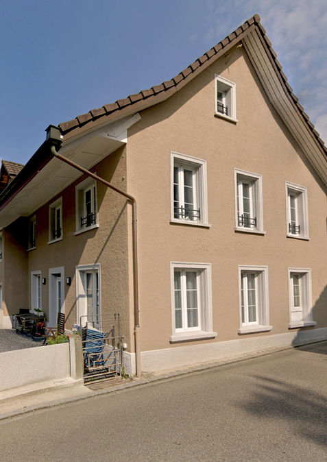 Ansicht Haus mit Satteldach und weiss umrahmten Fenstern