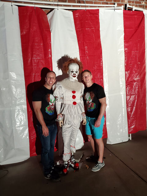 Dr. Brian Taillon and Dr. Steven Mueller, ECU Marketing professors and creators of the Haunted Halloween House yard display pose with Pennywise in front of a photobooth in Greenville, NC