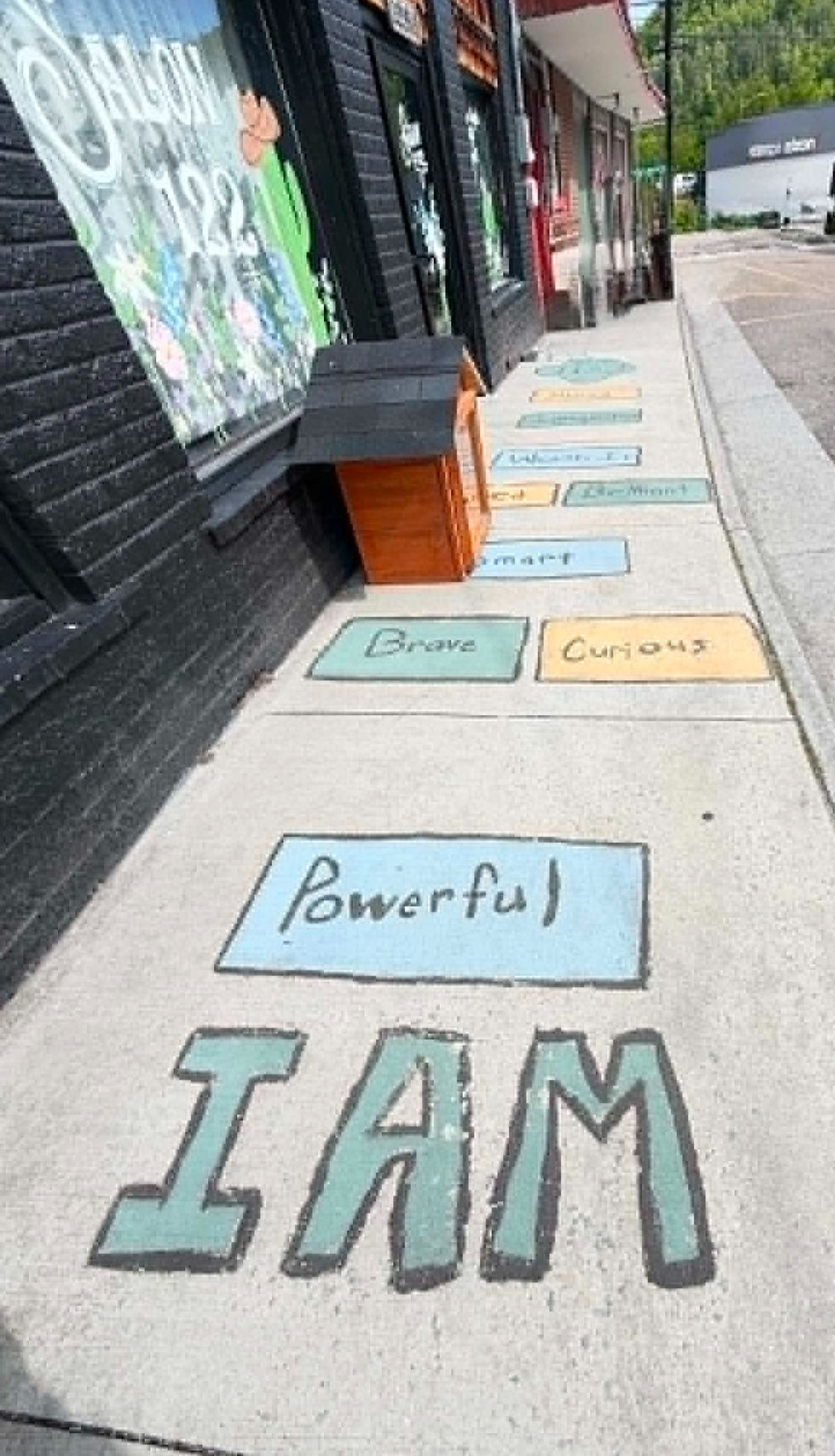 Colorful sidewalk with words like "Powerful," "Brave," and "Curious" outside "Salon 122" on a street. Positive and uplifting vibe.